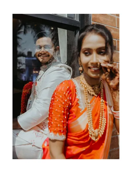 A creative engagement portrait, capturing the groom's reflection in a window as he smiles at his bride.