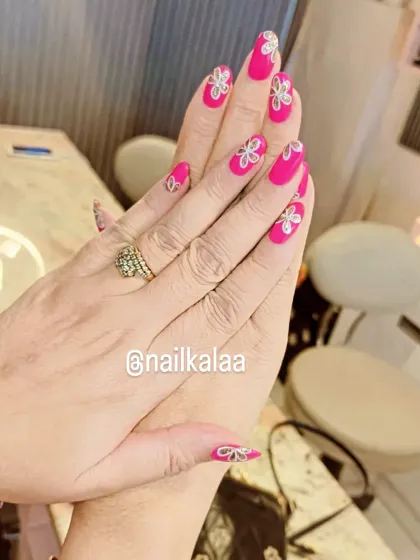 A bright pink manicure with delicate, hand-painted white and silver floral designs. This is a classic, feminine look with an artistic touch.