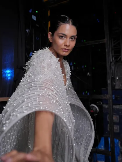 A backstage moment with model Bella for the Gaurav Gupta show. This candid shot captures the ethereal quality of the pearl-embellished cape and the clean, glowing makeup.