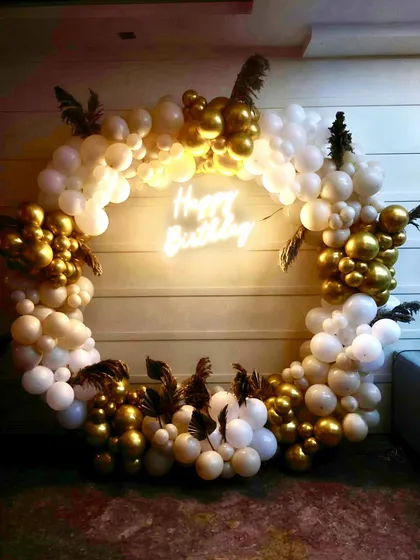 Elegance in every detail. This sophisticated birthday setup features a beautiful ring of white and gold chrome balloons, accented with delicate pampas grass and a warm 'Happy Birthday' neon sign for a touch of modern class.