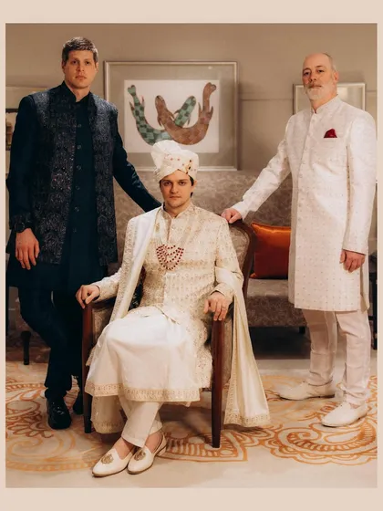 A formal, regal portrait of a groom seated in a chair, flanked by his father and another male family member. This black and white photograph has a classic, timeless quality, capturing three generations of men.