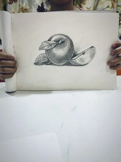 A student proudly shows their still life drawing of an apple, done with beautiful, soft shading.