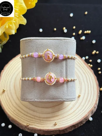A pair of delicate pink rakhis with a central charm and pearl accents. These are perfect for brothers who prefer a subtle and elegant design.