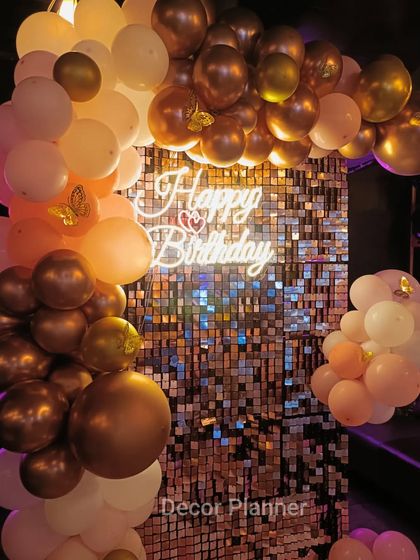 A detailed shot of the top of the balloon arch, showing the rich colors and the way the light from the neon sign reflects off the metallic balloons and sequin wall.