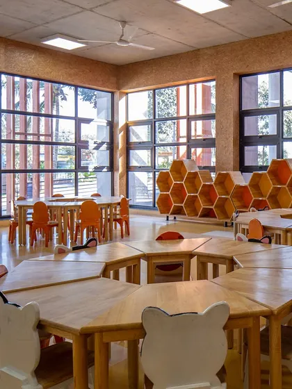 A classroom at Euro School, Bannerghatta, filled with natural light from large windows. The hexagonal tables and honeycomb shelving add a playful, geometric element while promoting collaborative learning.