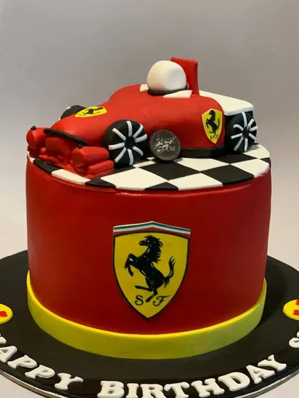 For the racing enthusiast, a custom Ferrari-themed birthday cake. This cake features a sculpted Formula 1 car on top of a red fondant base with the iconic Ferrari logo.