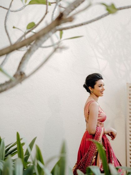 A beautiful candid of the bride, Jisha, walking through a garden, her pink lehenga vibrant against the green foliage.