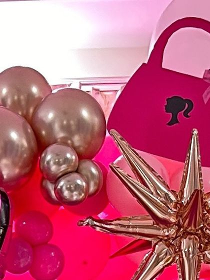 A close-up of a Barbie-themed balloon arrangement, featuring a pink handbag prop and a gold starburst foil balloon.
