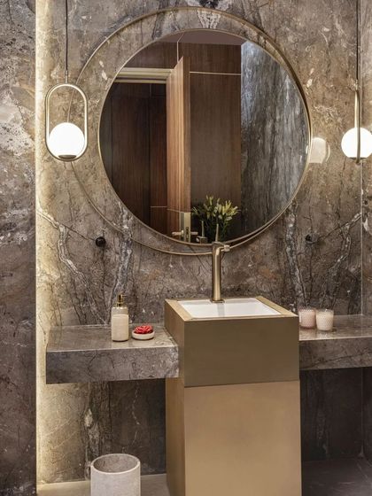 This powder room features a freestanding pedestal sink in brass and a dramatic grey marble wall. The round mirror and pendant lights create a focal point, showcasing luxury in a compact space.