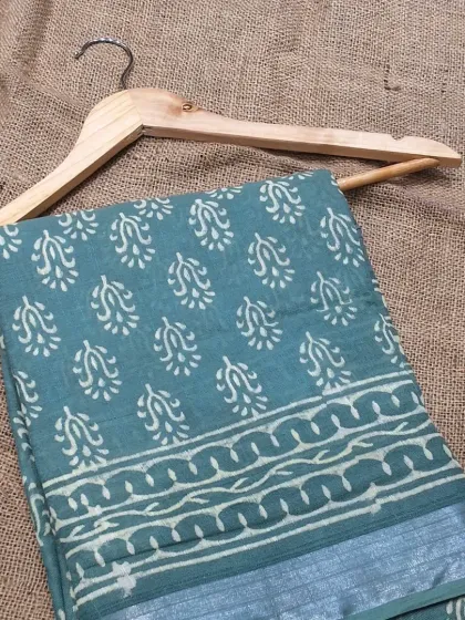 A cool-toned cotton linen saree in a shade of dusty teal. The simple block print and silver border make it an understated yet elegant choice for daily wear or casual events.