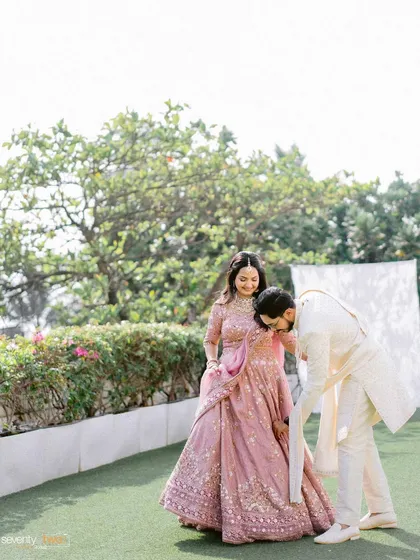 A sweet moment where the groom helps his bride with her lehenga, a candid gesture of care captured beautifully.
