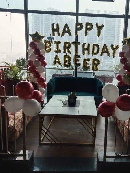 A simple and elegant birthday setup in a restaurant with a city view, featuring balloon pillars and foil letters.