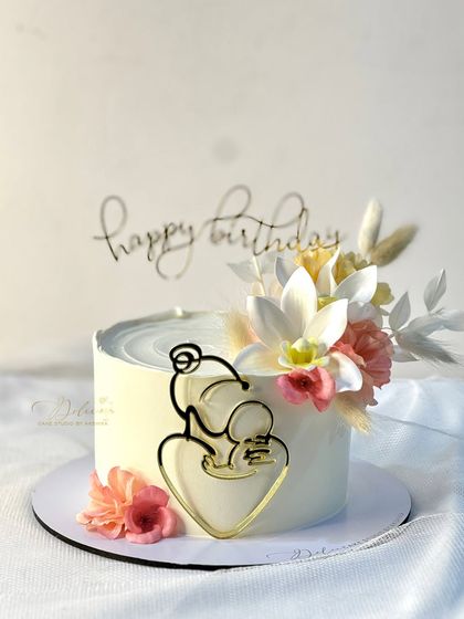 A beautiful cake for a new mother's birthday, featuring a "mother and child" topper and decorated with soft, dried flowers.