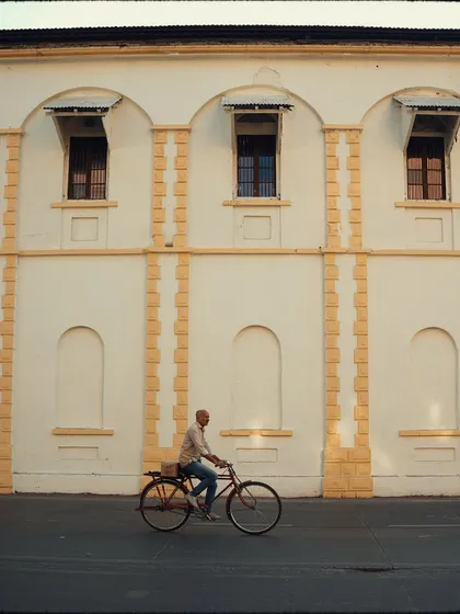 A man cycles past a building with beautiful, repeating architectural details. The clean composition and warm light create a simple, elegant street photograph.