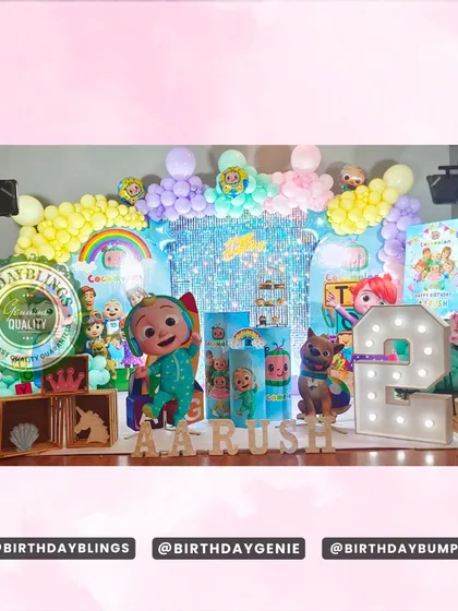 A vibrant Cocomelon party for a second birthday, featuring a full cast of characters on a stage with a shimmer wall. The setup includes themed plinths, a light-up number '2', and wooden name blocks.