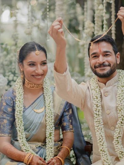 A joyful moment from a wedding ceremony, as the groom ties the sacred thread. The couple is surrounded by beautiful, understated floral decor.