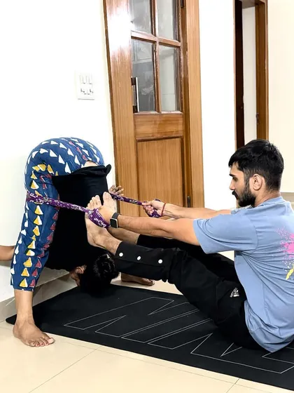 We use props like straps to make advanced poses like Kurmasana (Tortoise Pose) more accessible. Here, I'm using a strap to help my student gently pull her feet and deepen the forward bend.