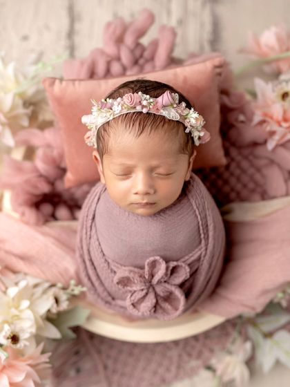 A beautiful angel in shades of pink. The floral wrap and headband add a touch of elegance to this peaceful newborn portrait.