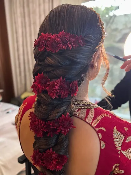 A stunning, thick bridal braid decorated with bands of red chrysanthemums for a bold and festive Christmas-themed wedding look.
