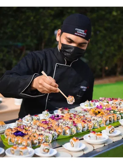A chef meticulously prepares a row of fresh sushi at a live station for a day reception. Our sushi bars are always a hit, offering guests a taste of authentic Japanese cuisine made right before their eyes.