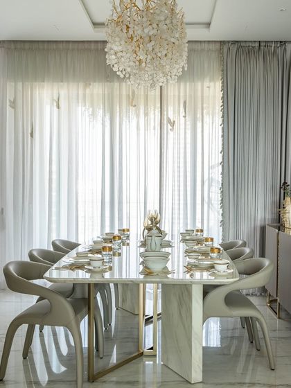 A formal dining room filled with light. The elegant space is defined by a large marble table, comfortable upholstered chairs, and a stunning crystal chandelier that adds a touch of sparkle.