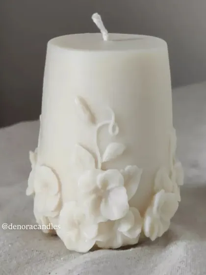A close-up of one of the floral pillar candles, showing the delicate 3D flowers at the base.