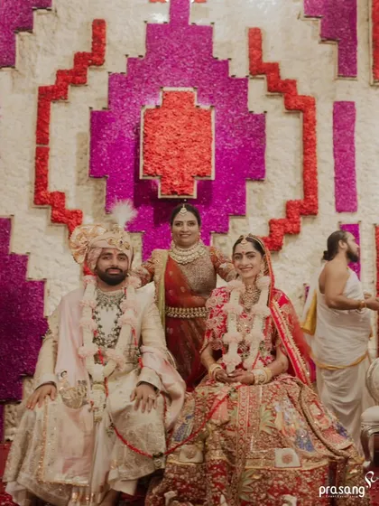 A formal portrait of the couple with a family member, seated before a stunning floral wall. I design these backdrops, like this one with a geometric pattern of red, pink, and white flowers, to serve as beautiful settings for family photos.