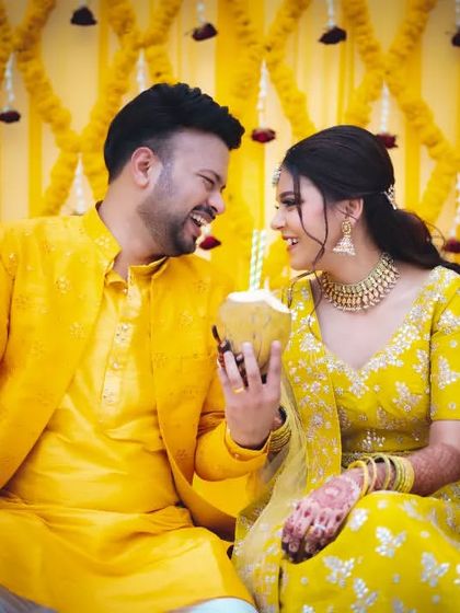 A sweet, candid moment where the couple shares a coconut drink during their Haldi ceremony, their smiles reflecting their happiness.