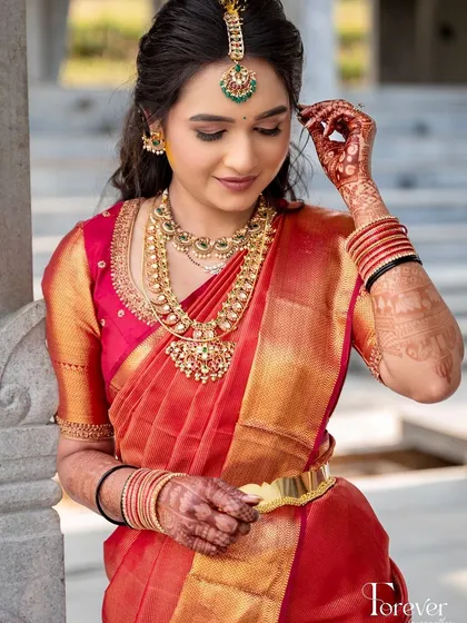 A close-up of a bride in her red Kanchipuram saree, showing the delicate embroidery on her blouse and her radiant smile.