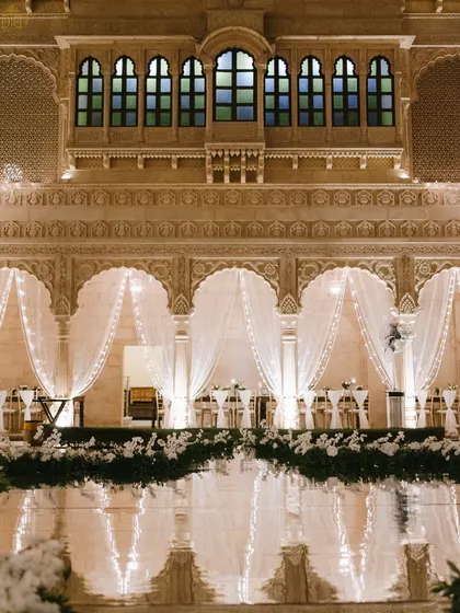 An all-white reception that exudes pure elegance. The historic courtyard of Suryagarh was transformed with flowing white drapes, fairy lights, and lush white florals, with the reflections in the water adding another layer of magic to the serene atmosphere.