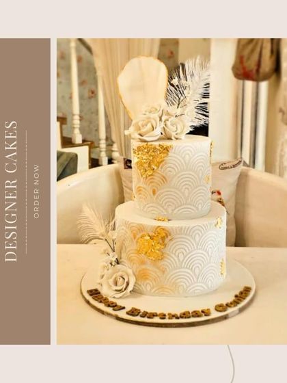 A stunning Art Deco-inspired two-tier cake in white and gold, featuring a geometric pattern, gold leaf, and elegant white sugar flowers.