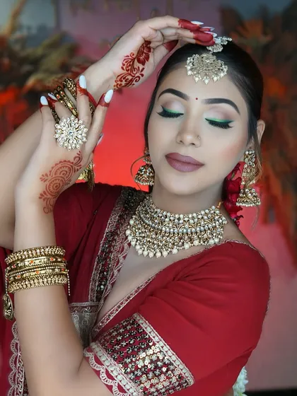 A classic red bridal look with a modern twist of a green winged eyeliner. This look combines traditional elements like henna and gold jewelry with contemporary makeup techniques.