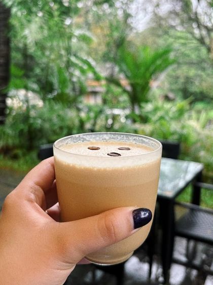An iced coffee against the lush green backdrop of Goa in the monsoon. This shot is all about the mood, capturing the feeling of a rainy, peaceful morning at a beautiful cafe.