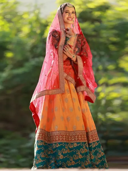 A full-length shot showing the complete Heeramandi-inspired lehenga with its red, yellow, and teal green panels. The model's pose with the dupatta creates a classic, graceful silhouette.
