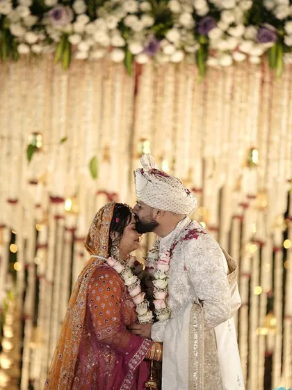 A tender kiss on the forehead after the varmala exchange. The backdrop of hanging floral strings adds a delicate and romantic texture to this beautiful moment.