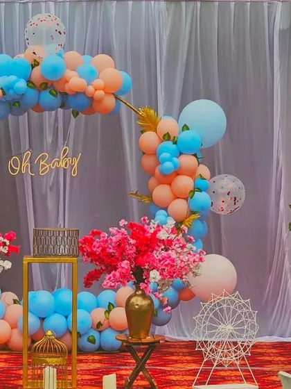 A vibrant and colorful "Oh Baby" setup. This design features a circular frame with a blue and peach balloon garland and a decorative birdcage filled with flowers, adding a whimsical touch.