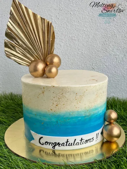 An elegant congratulations cake with a blue ombre effect and gold dust. The design is finished with a gold palm spear and spheres.