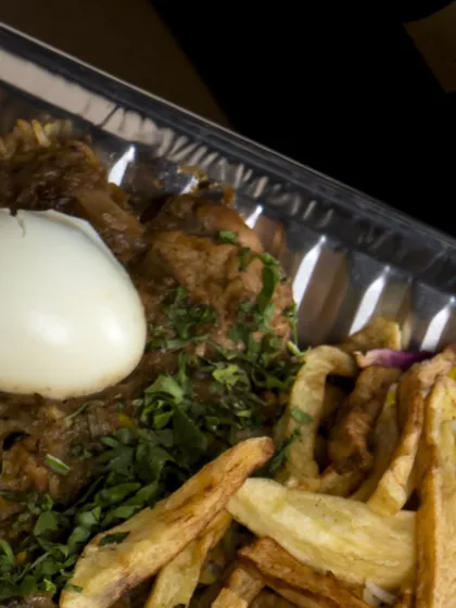 Another angle of a party-sized biryani tray, this one topped with crispy fries, boiled eggs, and fresh herbs. A complete meal in one tray.