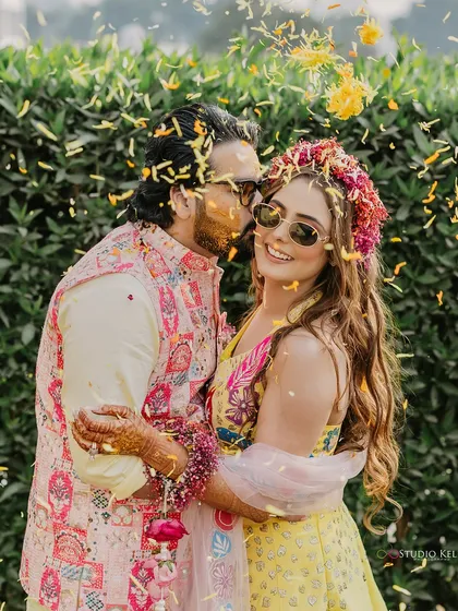 A sweet, candid moment with the groom kissing the bride's cheek amidst a shower of petals during their Haldi ceremony.