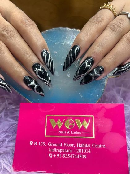 A fierce and edgy design on long, stiletto nails. This look features a black base with 3D chrome silver abstract patterns, creating a futuristic and powerful vibe.