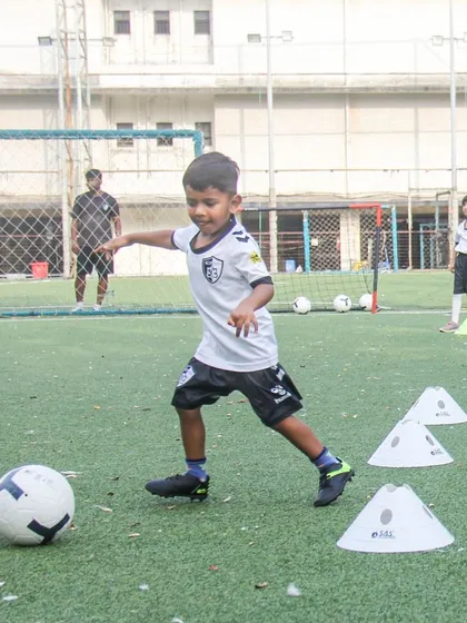 A young player dribbles through a series of cones, demonstrating the focus and coordination we build through our age-specific training programs.