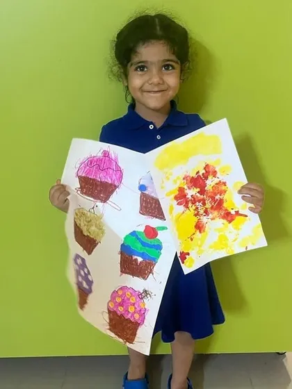 So proud of her creations! This student is holding up her cupcake collage and another abstract painting, showing the variety of art we explore in the studio.