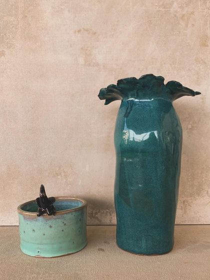 A set of two handmade vases, one a tall, glossy green piece and the other a smaller, speckled cup with a tiny black star. They look beautiful together or on their own.