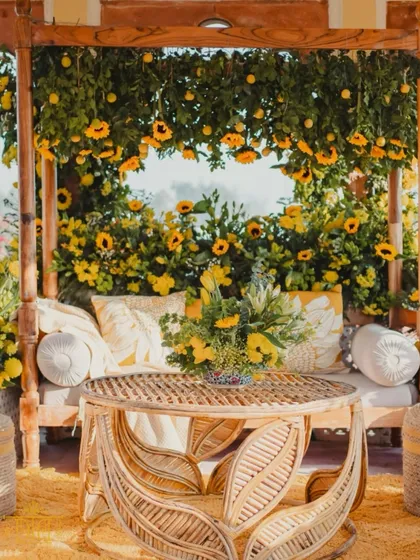 A cheerful and sunny Haldi seating area, featuring a swing decorated with sunflowers and lemons. The rattan furniture and yellow-themed cushions create a relaxed, bohemian vibe perfect for a daytime celebration.