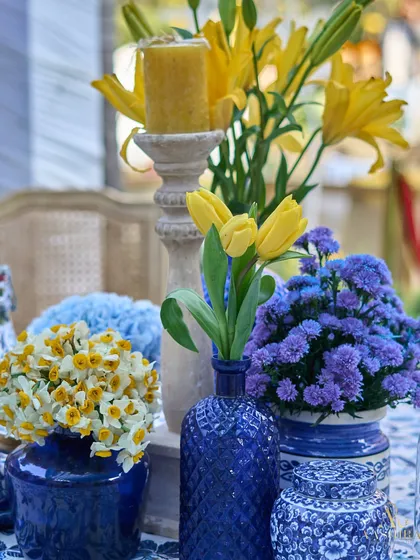 A close-up of the blue and yellow floral centerpiece, featuring yellow tulips, daffodils, and blue hydrangeas in patterned vases.
