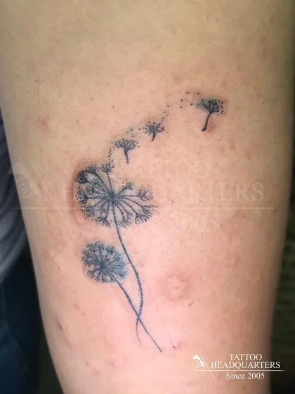 A delicate dandelion tattoo with its seeds blowing away in the wind, symbolizing letting go and making wishes.