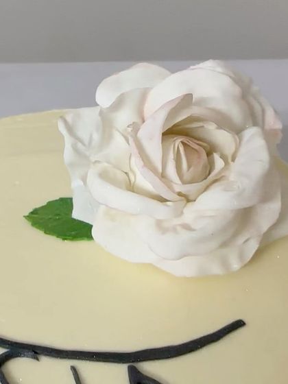 A close-up of the delicate, handmade white sugar rose that sits atop the piano-themed cake. Each petal is carefully shaped by hand.