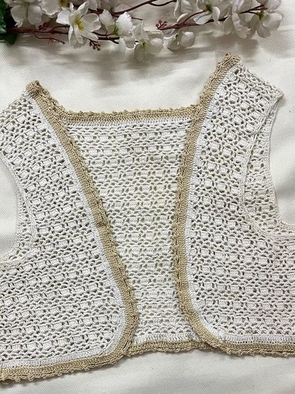 A closer look at our sleeveless shrug in white with a beige border. It's a simple and elegant piece to layer over tops and dresses.