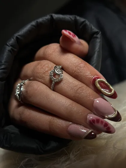A chic and modern set of polygel extensions with a deep red and nude color palette and gold chrome accents.