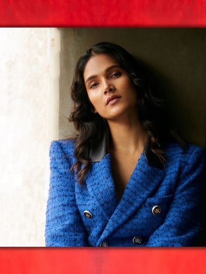 A close-up portrait that highlights the texture of a blue tweed blazer. The styling is simple and confident, letting the rich fabric and the model's direct gaze command the frame.